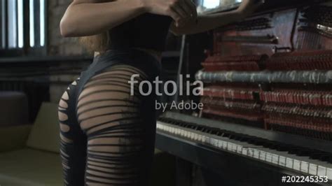 Beautiful girl is dancing twerk in a hall near a piano ...